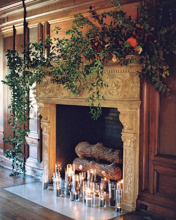 a vintage refined fireplace with dark candles, firewood and lush foliage on the mantel
