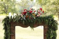 18 a chic rustic mantel with a lush evergreen garland, white candles and a lush red floral centerpiece