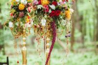 18 a vibrant wedding centerpiece with pink, red, yellow and orange blooms, greenery, feathers and candles
