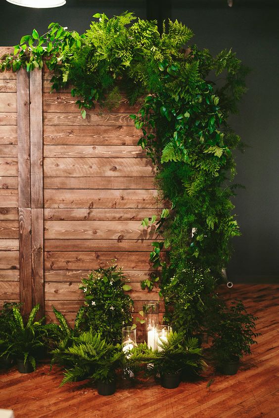 a wedding backdrop of wood decorated with ferns and other greenery, with candles around