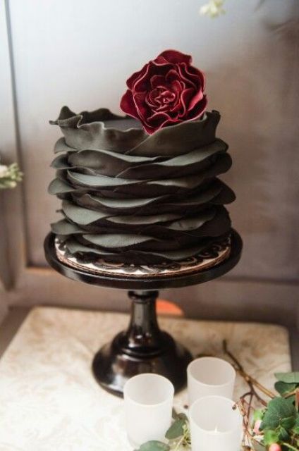a dramatic black fondant ruffle wedding cake with a red sugar flower on top for a moody wedding