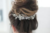 21 a dimensional messy top knot is accented witha  large pearly hairpiece for a more refined feel