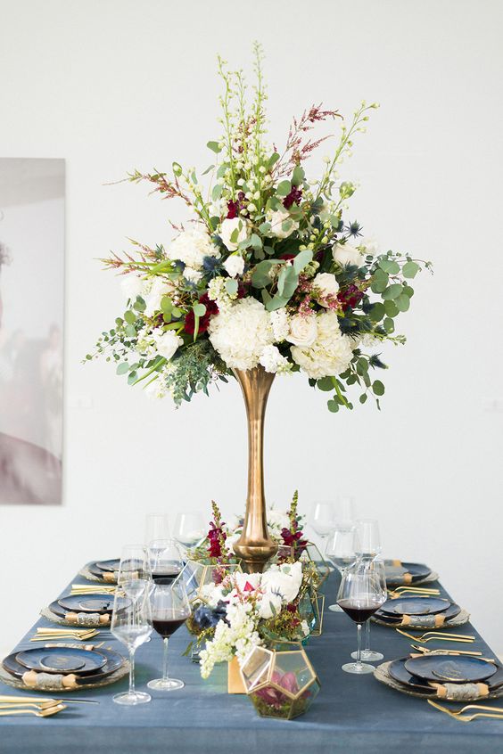 an elegant wedding centerpiece of white, burgundy blooms, thistles and eucalyptus in a brass tall vase