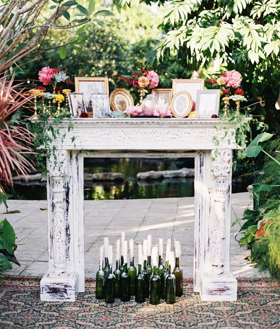 a shabby chic white mantel with lots of candles in the bottles, photos in frames and bright blooms