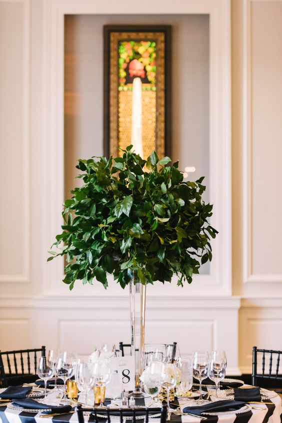 an ultra-modern tall centerpiece of a clear vase and foliage looks amazing and follows the non-floral wedding trend