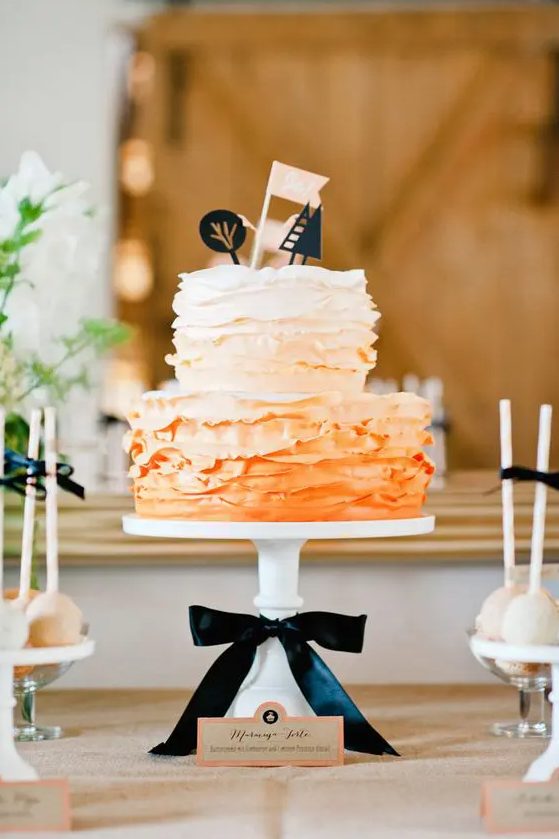 a bold and bright ruffle ombre orange wedding cake with fun black cake toppers, a flag and a black bow is a bold idea for a modern wedding