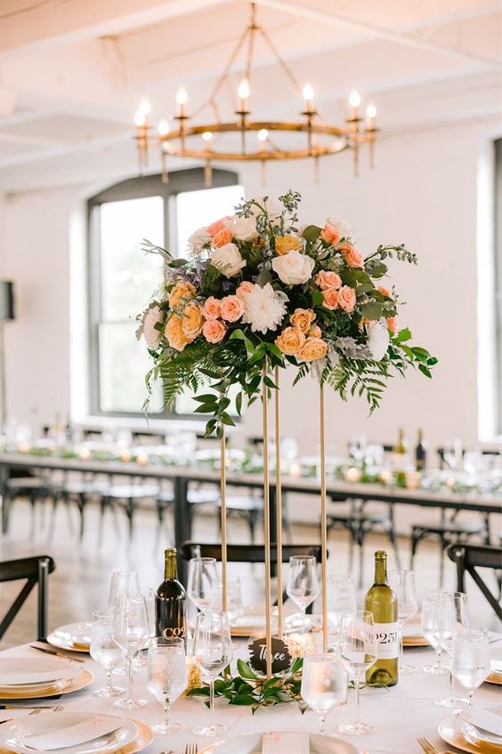 a chic tall summer wedding centerpiece of white dahlias, peachy and pink roses and lots of dimensional greenery and leaves