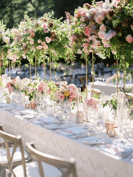 a chic wedding tablescape with pink floral centerpieces and matching tall centerpieces with much greenery and dark and pink blooms