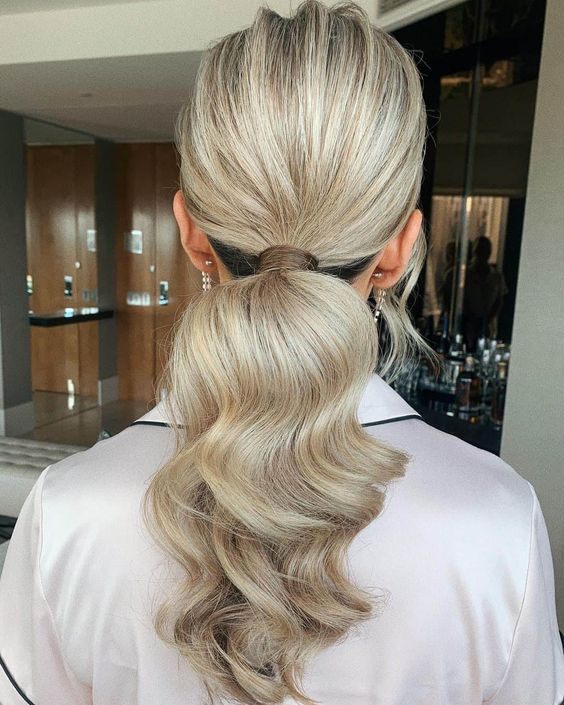 a cool low modern ponytail with a volume on top and wavy hair down is a cool idea for a modern wedding guest