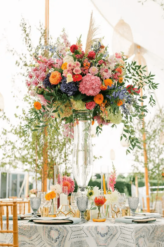 a gorgeous tall wedding centerpiece of blush, pink, orange, violet and blue flowers and greenery for a summer wedding