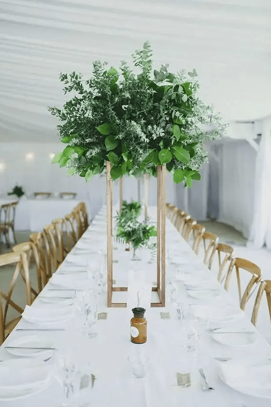 a gorgeous tall wedding centerpiece of lush and textural greenery on a copper stand