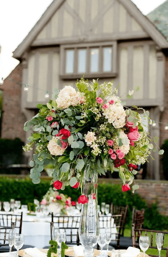 a lush statement wedding centerpiece in a clear vase, with blush, pink and red blooms and greenery is amazing
