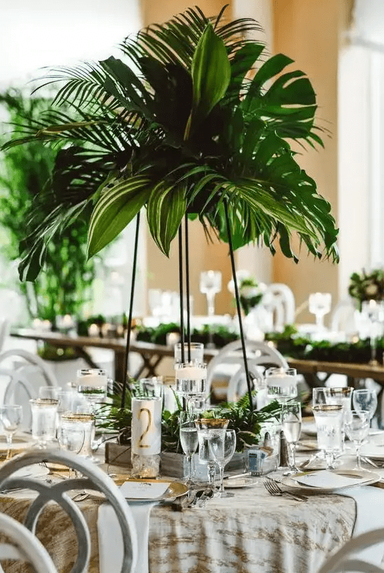 a lush tropical wedding centerpiece of tropical leaves on a tall black metal stand and a matching decoration on the table