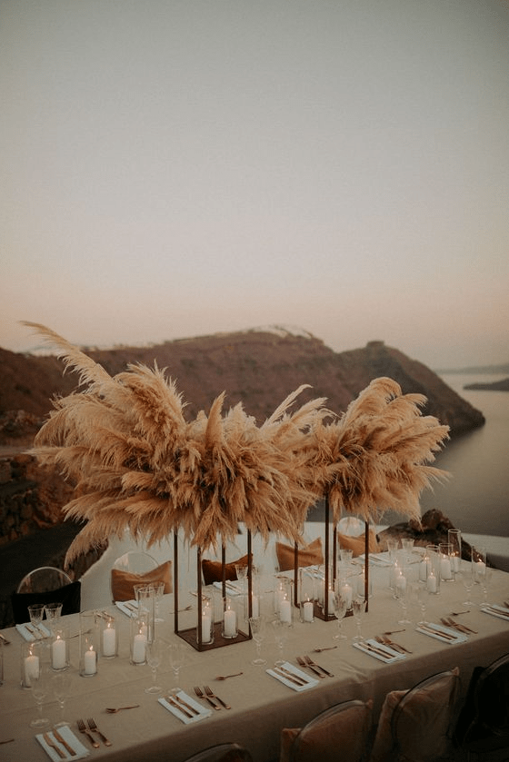 a lush wedding centerpiece of lots of pampas grass on tall stands and candles lining up the table for a boho wedding