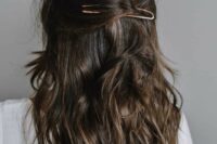 a messy half updo with waves down and a large hair pin is a stylish idea for a modern or boho wedding guest
