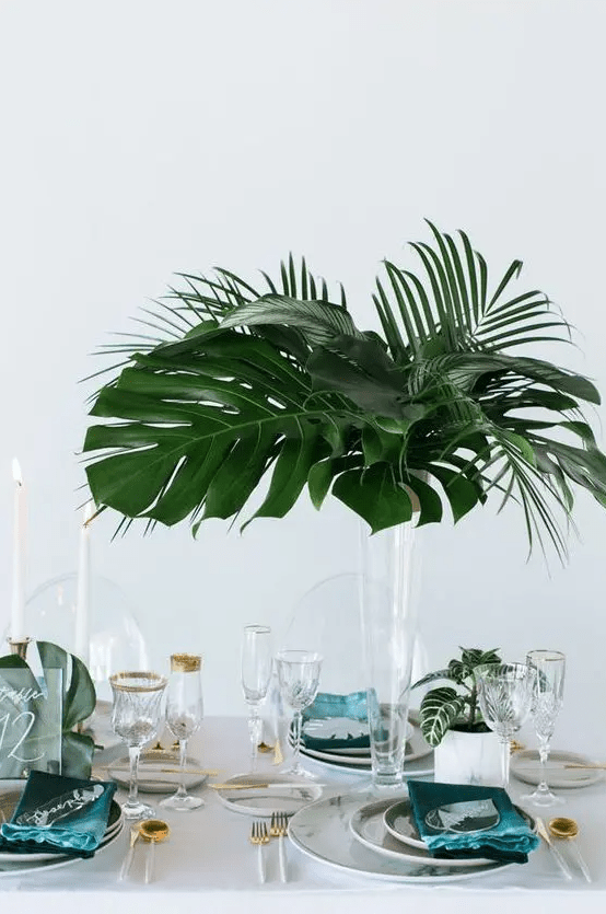 a minimalist tropical wedding centerpiece with a tall clear vase and some cute tropical leaves is a chic idea for a minimal wedding