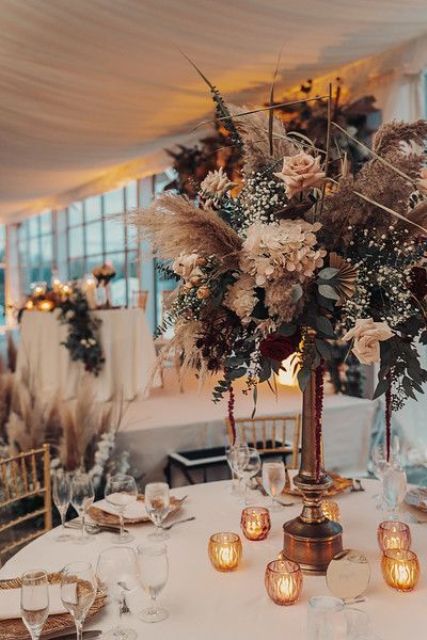 a quirky tall wedding centerpiece of white hydrangeas, blush roses, greenery, baby’s breath, pampas grass and amaranthus