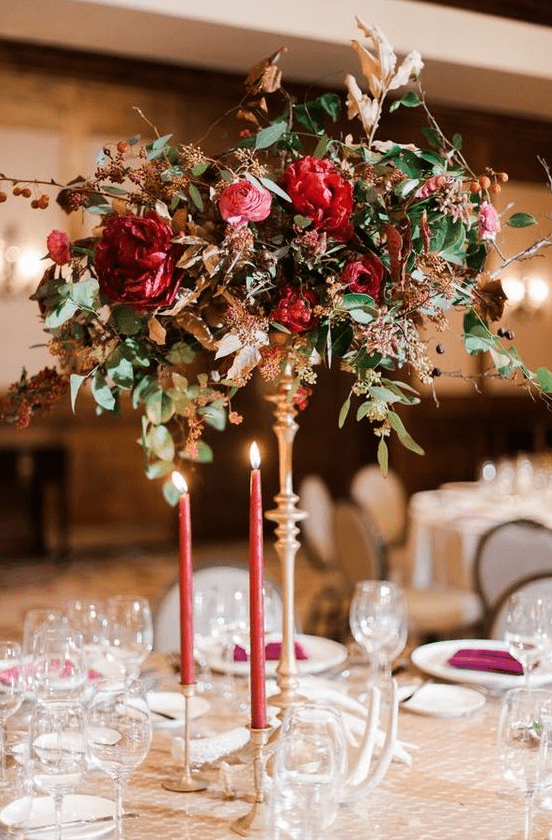 a refined and bright tall wedding centerpiece of a deep red, pink arrangement with greenery and berries on branches