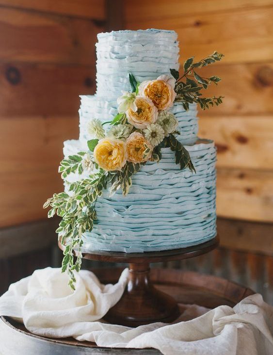 a ruffle powder blue wedding cake decorated with greenery and neutral and rust blooms
