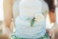 a ruffled ombre wedding cake from white to blue, with greenery and a neutral flower for a beach or coastal wedding