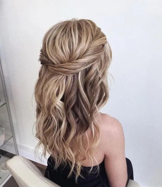 a simple and catchy textured wavy half updo with a twisted halo and a bump on top is a cool and chic idea for a wedding