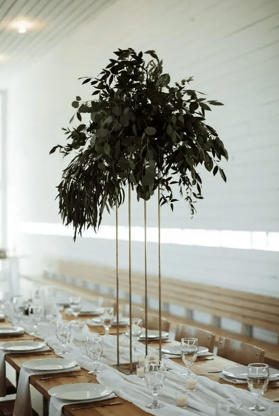 a tall minimalist wedding centerpiece on a gilded stand and with lush textural greenery won’t take much table space