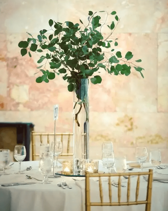 a tall silver eucalyptus centerpiece in a clear vase is an ultra-modern idea of wedding decor