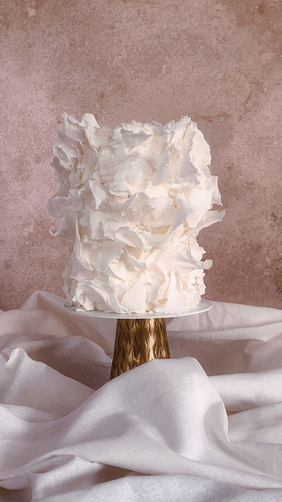 a whimsical ethereal white wedding cake all covered with ruffles looks absolutely adorable