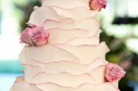 a white layered wedding cake with pink edges and pink roses is a chic idea for spring or summer