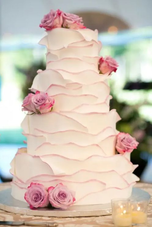 a white layered wedding cake with pink edges and pink roses is a chic idea for spring or summer