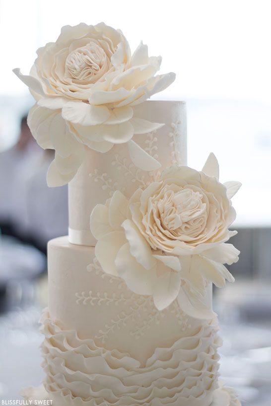 a white pattern wedding cake with ruffles topped with oversized white sugar blooms is a very sophisticated idea