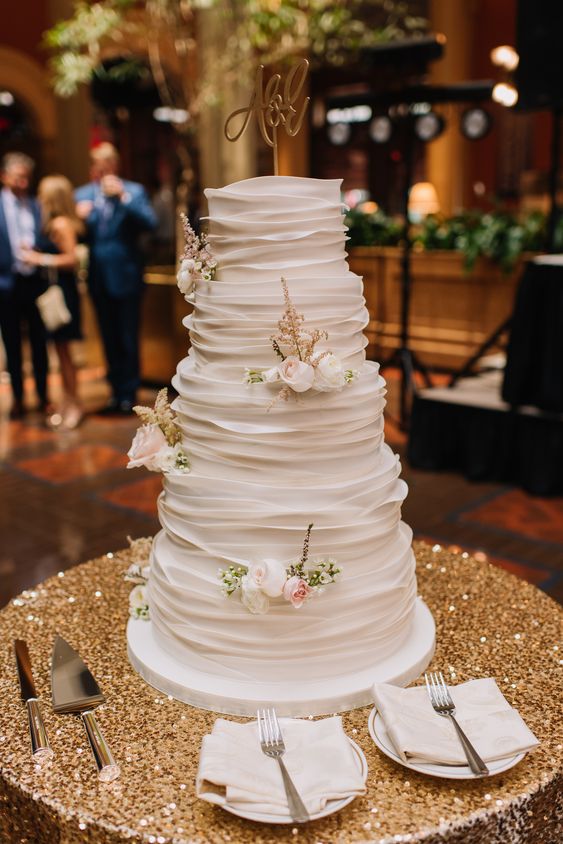a white ruffle wedding cake topped with fresh neutral blooms and a calligraphy cake topper looks very elegant