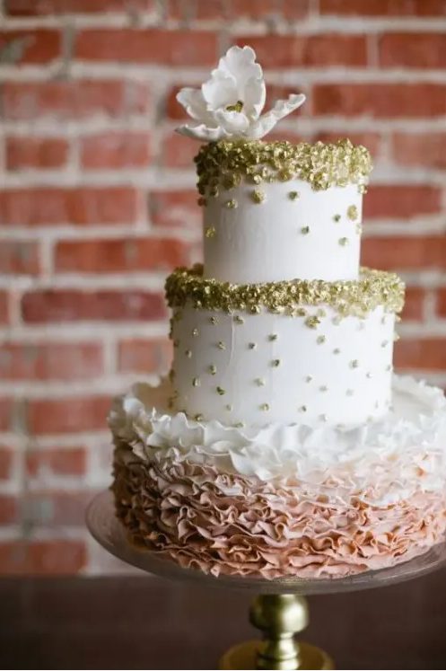 a white textural wedding cake with gold leaf and an ombre ruffle tier plus a white sugar bloom on top