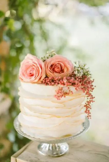 a white tiered wedding cake with copper edges, pink and white blooms, greenery and berries is amazing for spring or summer