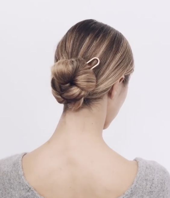 an elegant braided low bun with a sleek top and a large hair pin is a stylish and cool modern hairstyle