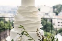 an elegant white wedding cake with polka dot and ruffle tiers, white blooms and greenery on top is very chic and cool