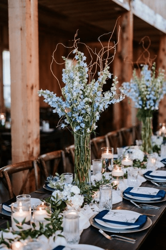 an indoor spring wedding reception with pastel blue centerpieces and runners of greenery and white blooms and candles