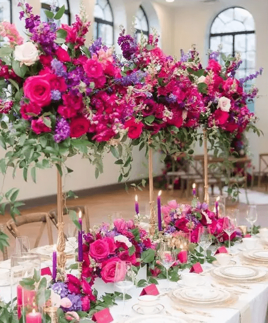Tall jewel tone centerpieces with hot pink, purple and violet blooms and greenery and matching table runners and purple candles