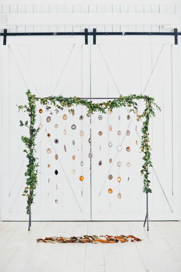 a creative greenery arch with agate slices hanging gown and some leaves under the arch for a boho ceremony
