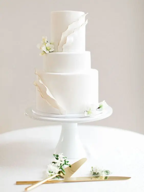 a chic white wedding cake with textural touches and gold edging plus fresh white flowers, modern classics
