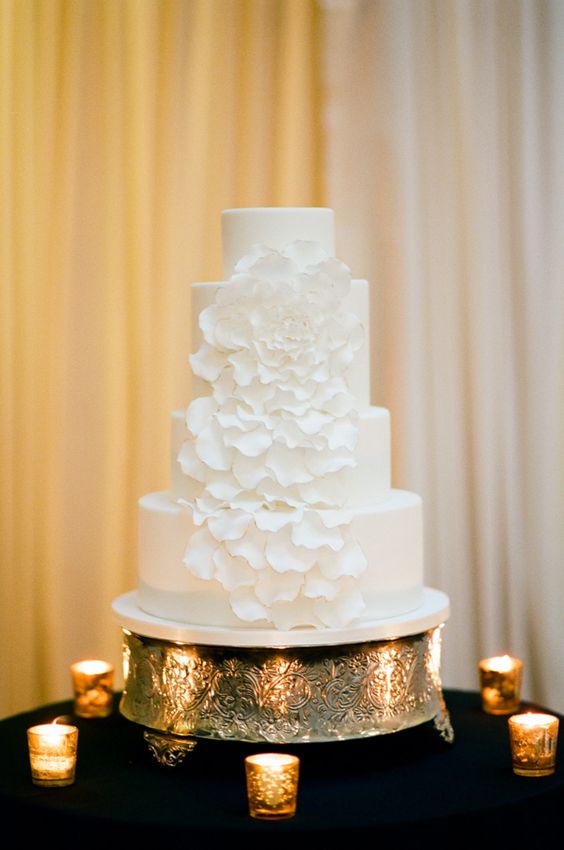 a plain white wedding cake decorated with a large white sugar flower, the petals are cascading for a whimsy touch