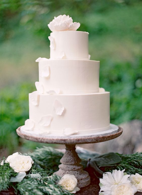 a gorgeous white wedding cake with white sugar flowers and petals falling down for a wow effect