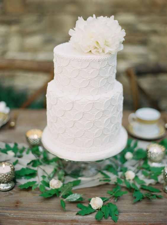 a textural white wedding cake with a floral pattern and a white white bloom on top looks vintage-like and chic