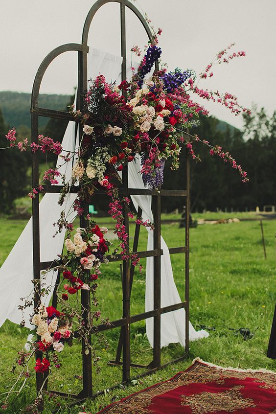 a forged frame decorated with airy fabric and lush colorful blooms plus a Persian rug for a dreamy outdoor ceremony
