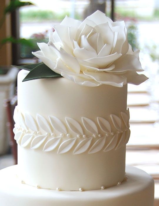 a white wedding cake with sugar leaves and a giant flower plus edible pearls is pure elegance with a modern twist
