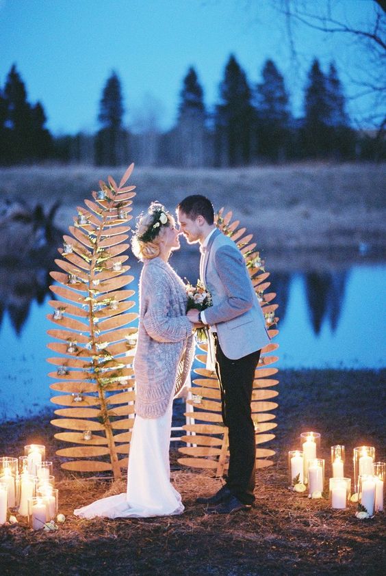 a nature-inspired wedding backdrop of two wooden fern leaves decorated with greenery and with candles around