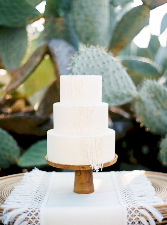 an all-white wedding cake decorated with macrame is great for desert or boho weddings