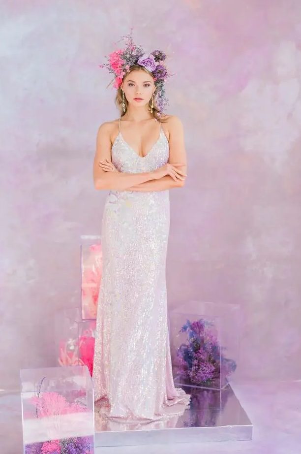 a bride wearing a white sequin spaghetti strap wedding dress, a lilac and pink iridescent floral crown and matching florals in clear cubes around