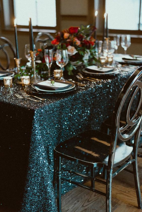 a chic NYE wedding tablescape with a teal sequin tablecloth, black candles, bold blooms and chic cutlery and plates