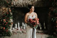a chic strapless lace sheath wedding dress with a train and carrying a red and pink wedding bouquet